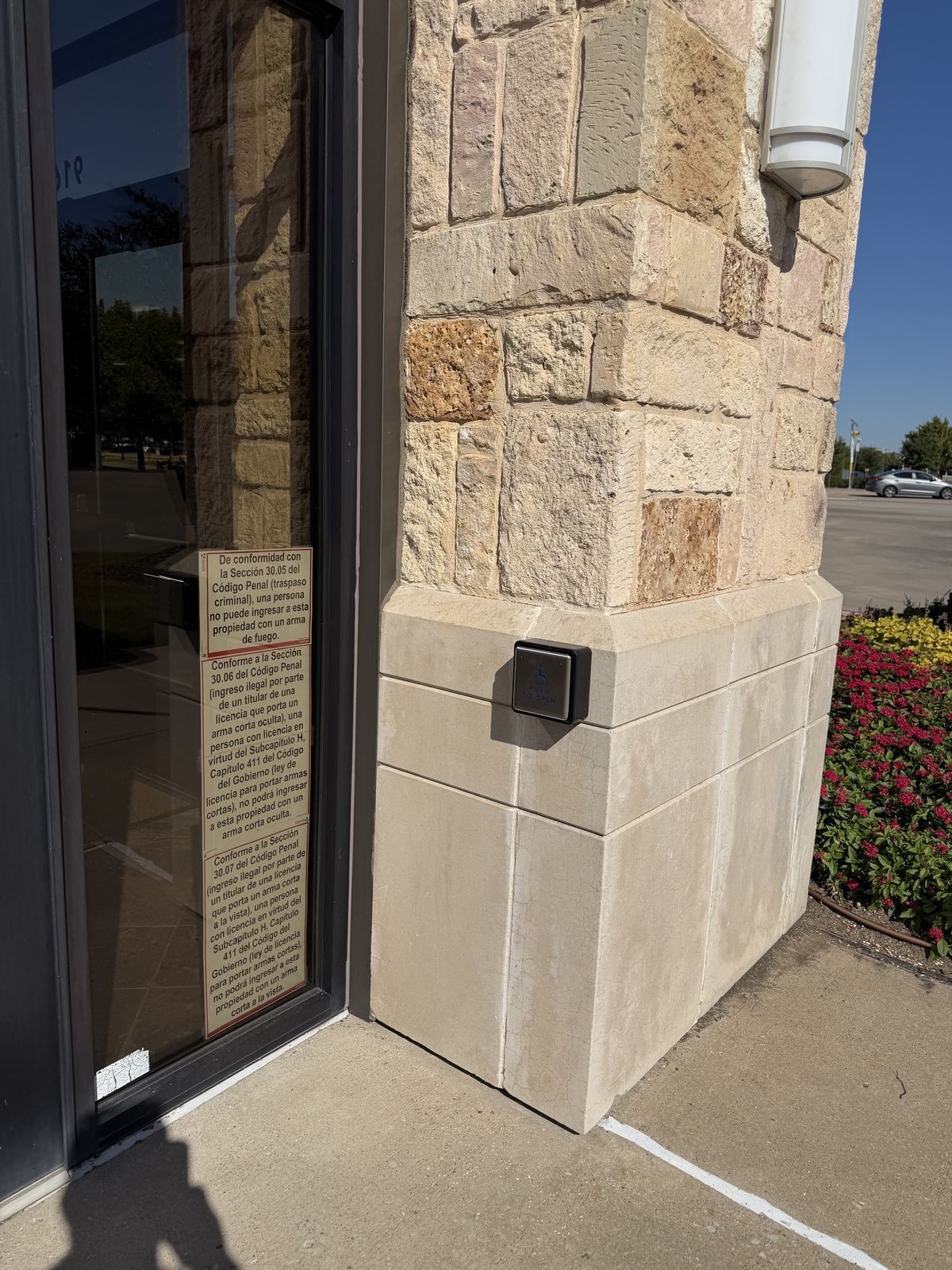 Square push button for an automatic door mounted on a stone column outside a glass storefront entrance