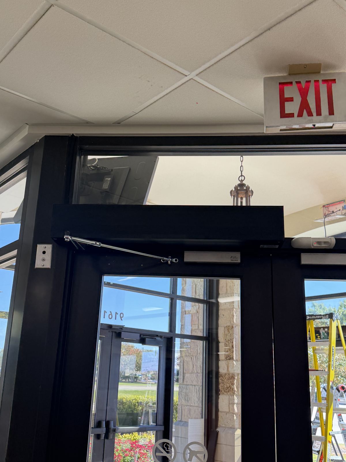 Dark bronze double entry doors with an automatic door operator across the top, seen from inside the vestibule