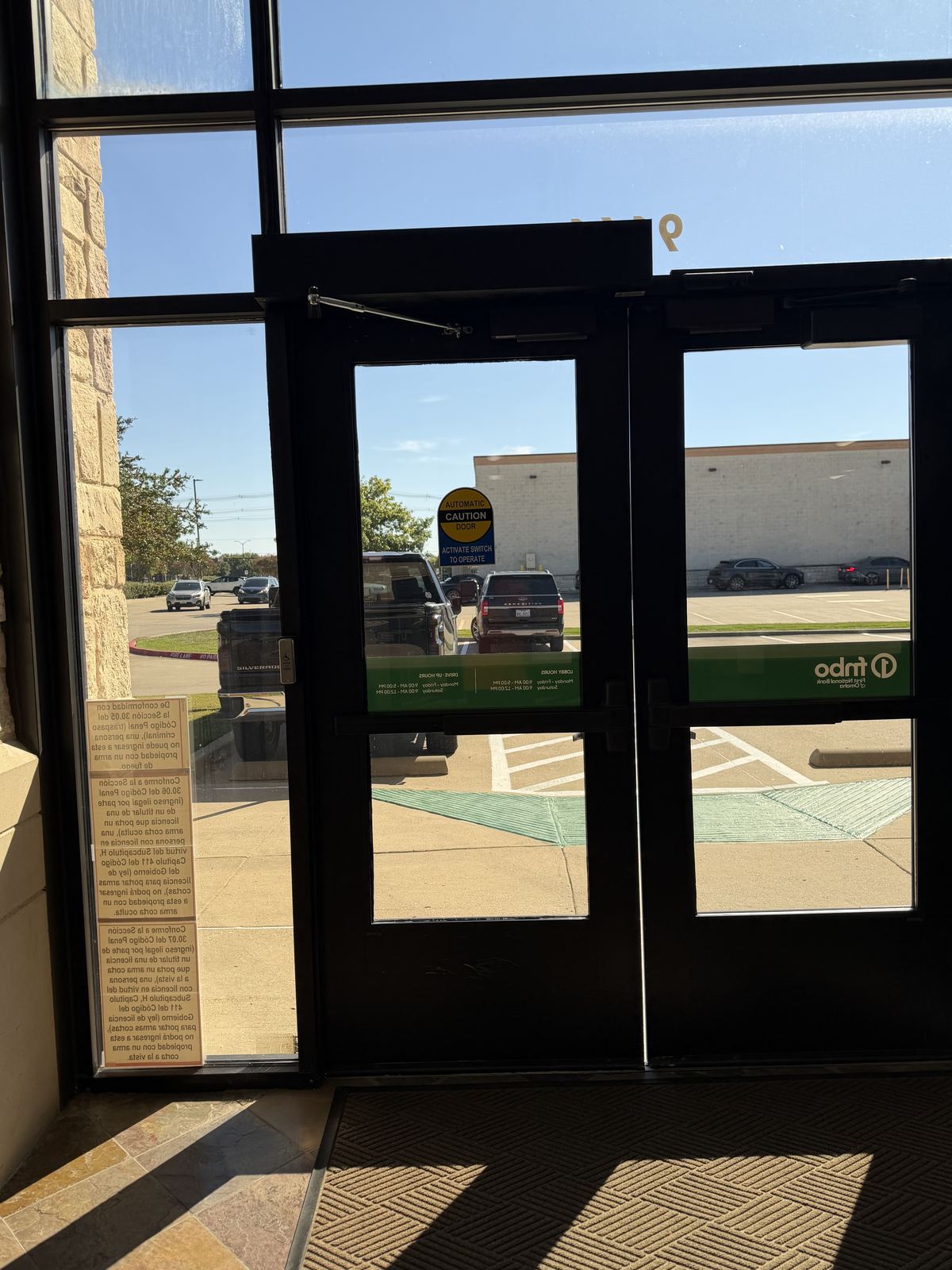 Pair of dark bronze aluminum storefront doors with an automatic operator above them, looking out to a parking lot