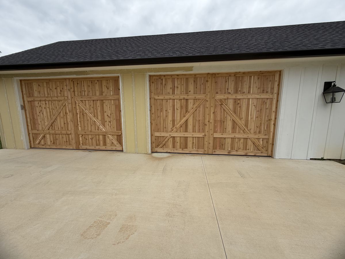 Two cedar carriage-style garage doors with X-brace detail on a board-and-batten building