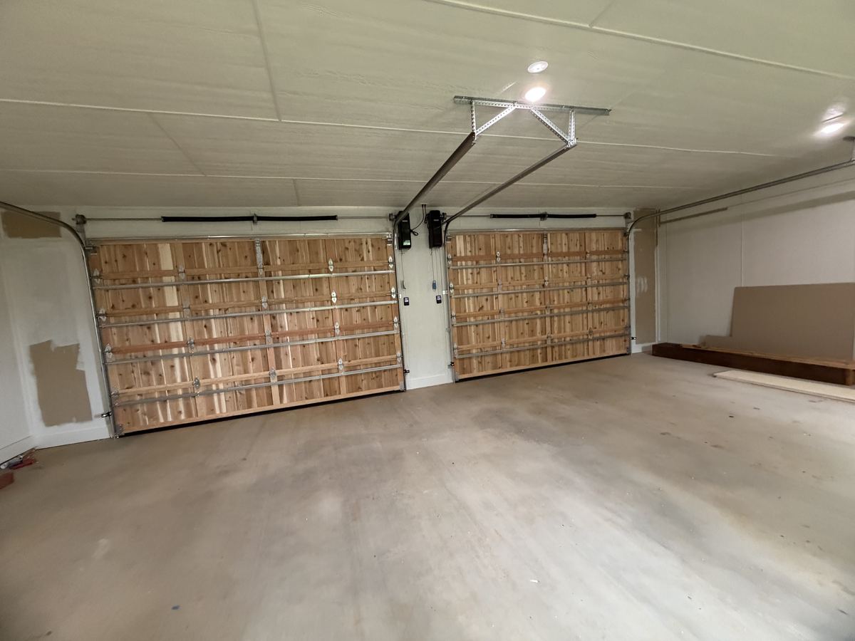 Inside view of two cedar overhead garage doors with tracks, springs and openers mounted to the ceiling
