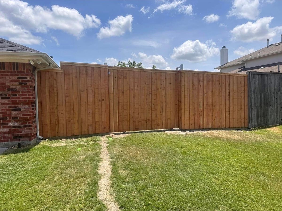 New cedar privacy fence with a top cap and trim boards beside a brick home