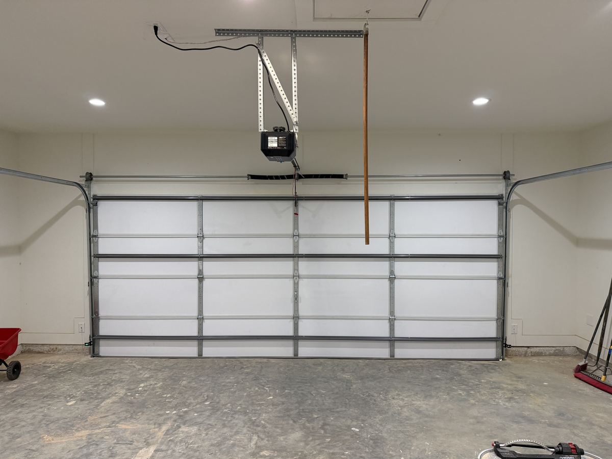 Inside view of a white insulated garage door with an opener and steel struts across the panels