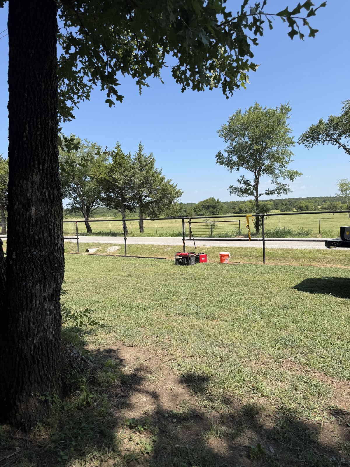 Metal pipe fence along a rural road frontage, with a generator and tools set up on the grass