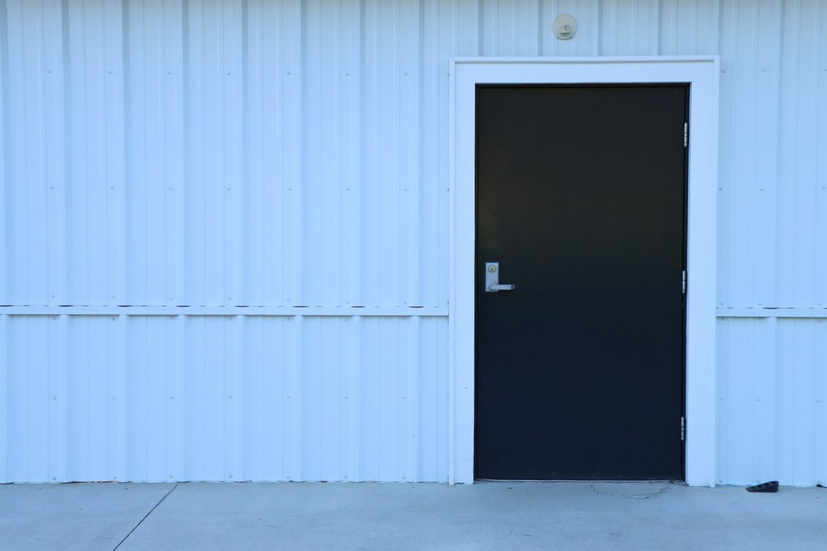 Black steel service door with a lever handle set in a white corrugated metal wall