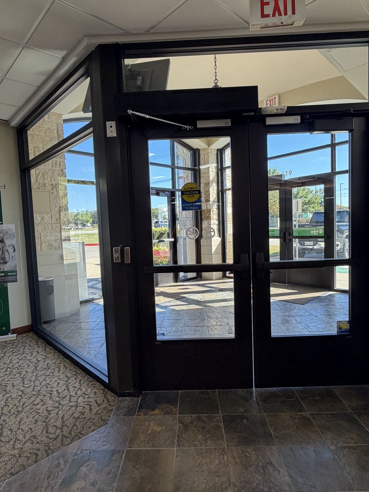 Wide view of a storefront vestibule with dark bronze double entry doors and an automatic operator header