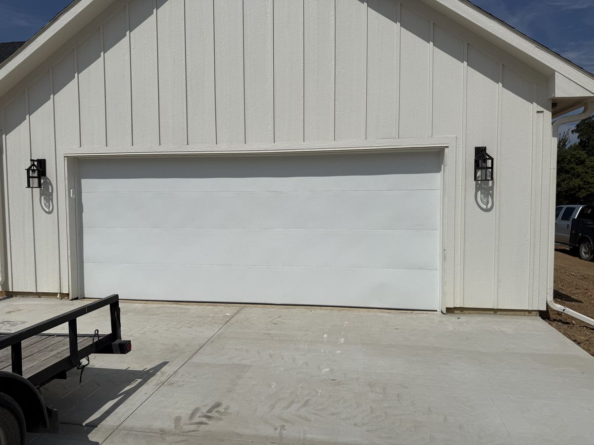 White flush-panel garage door on a white board-and-batten home with black lantern lights on each side